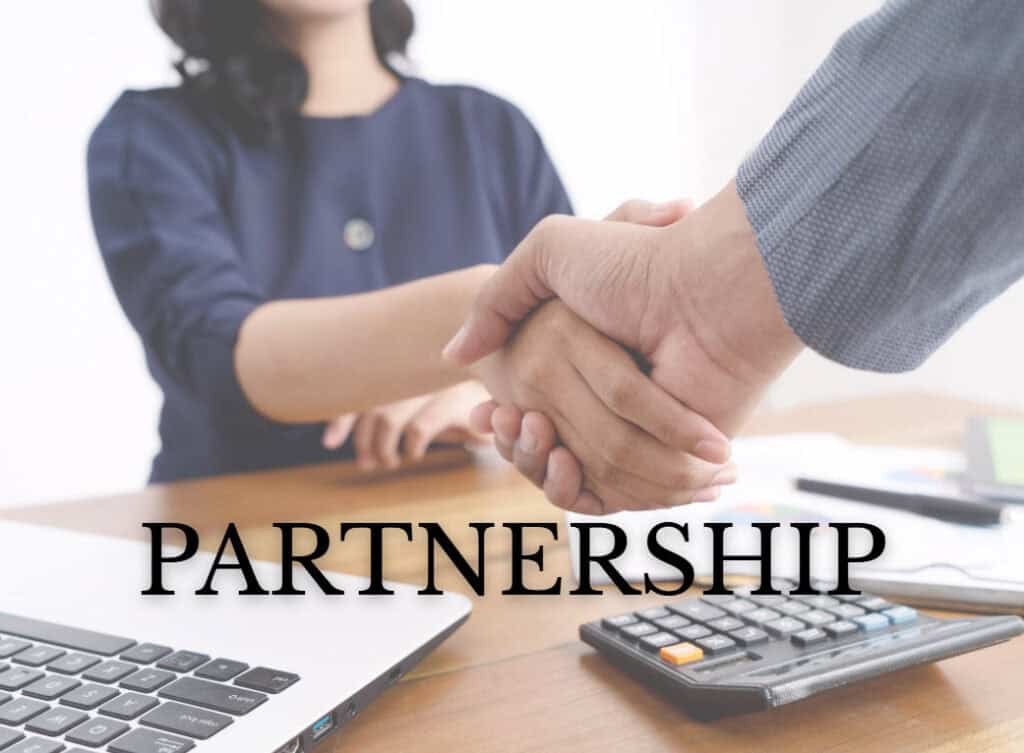 Two people shake hands across a desk with a laptop and calculator in view, symbolizing a business agreement. The word “PARTNERSHIP” is prominently displayed in bold black letters across the image.