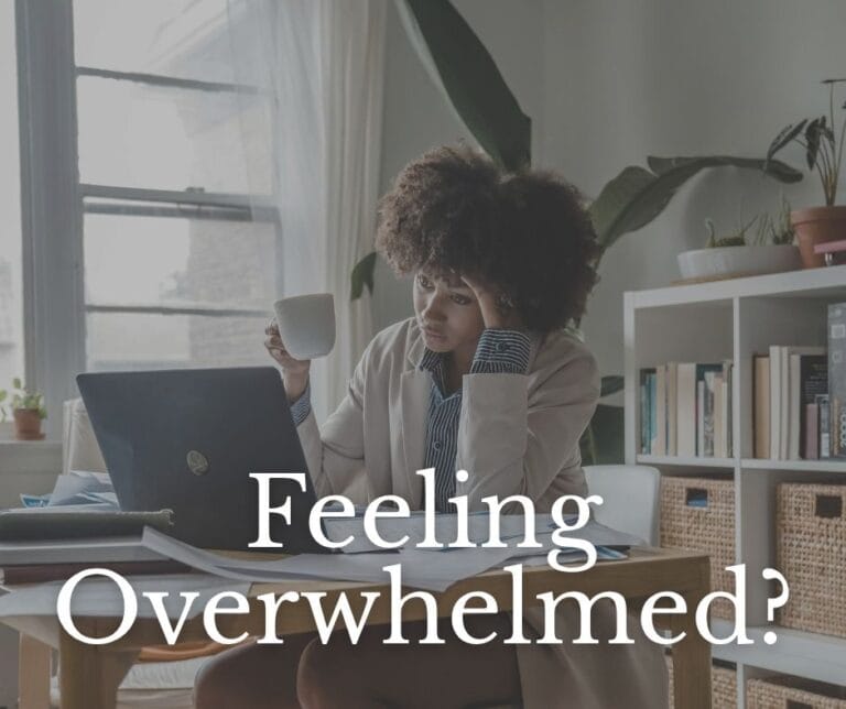 A woman sits at a cluttered desk with a laptop and papers, holding her head in one hand and a coffee mug in the other, looking stressed. The text overlay reads “Feeling Overwhelmed?” suggesting emotional or mental burnout in a home office setting.
